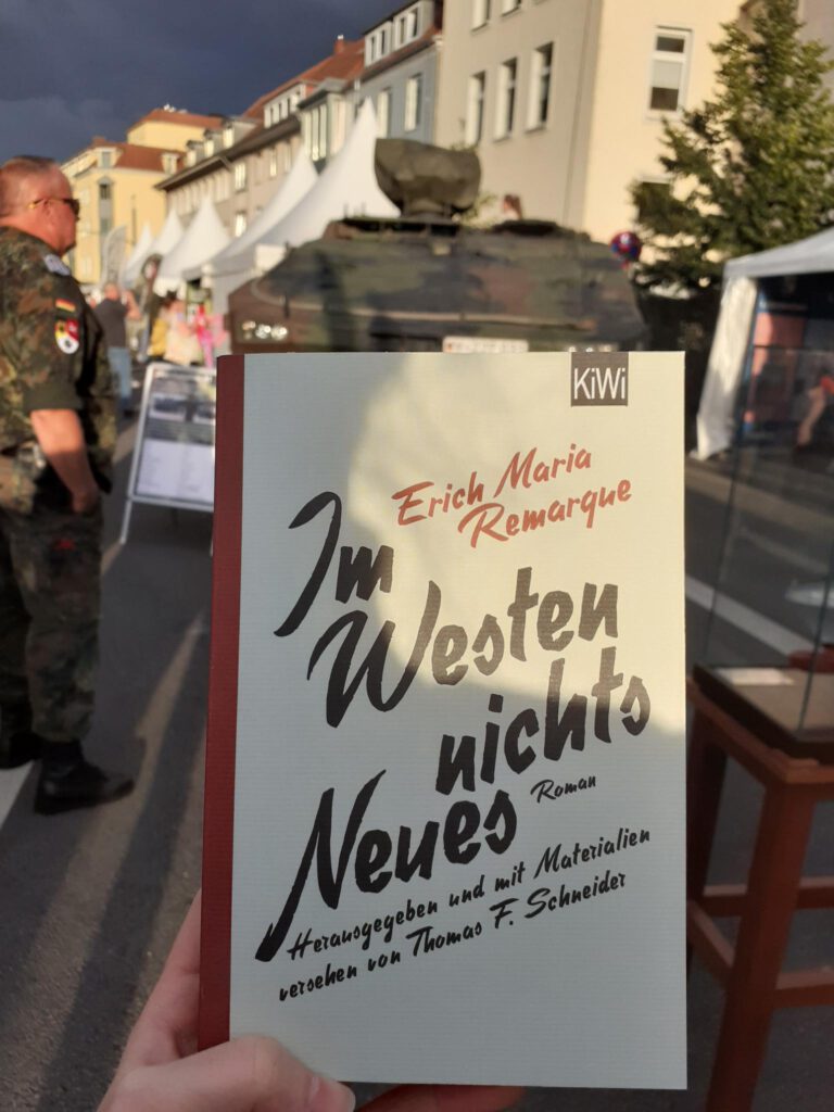 Das Buch "Im Westen nichts Neues". Im Hintergrund ist ein Panzer der Bundeswehr zu sehen.