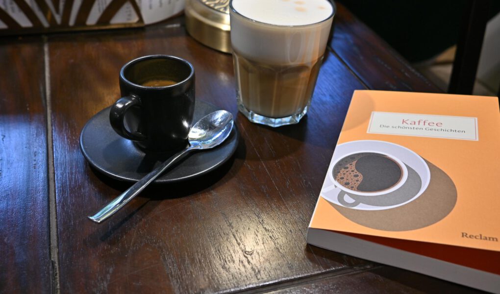 Ein Foto einer Tasse Espresso neben dem Buch "Kaffee" aus dem Reclam Verlag auf einem Café-Tisch