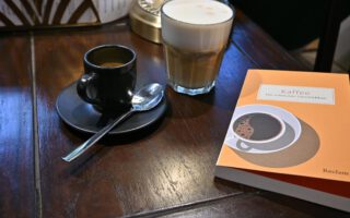 Ein Foto einer Tasse Espresso neben dem Buch "Kaffee" aus dem Reclam Verlag auf einem Café-Tisch