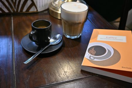 Ein Foto einer Tasse Espresso neben dem Buch "Kaffee" aus dem Reclam Verlag auf einem Café-Tisch